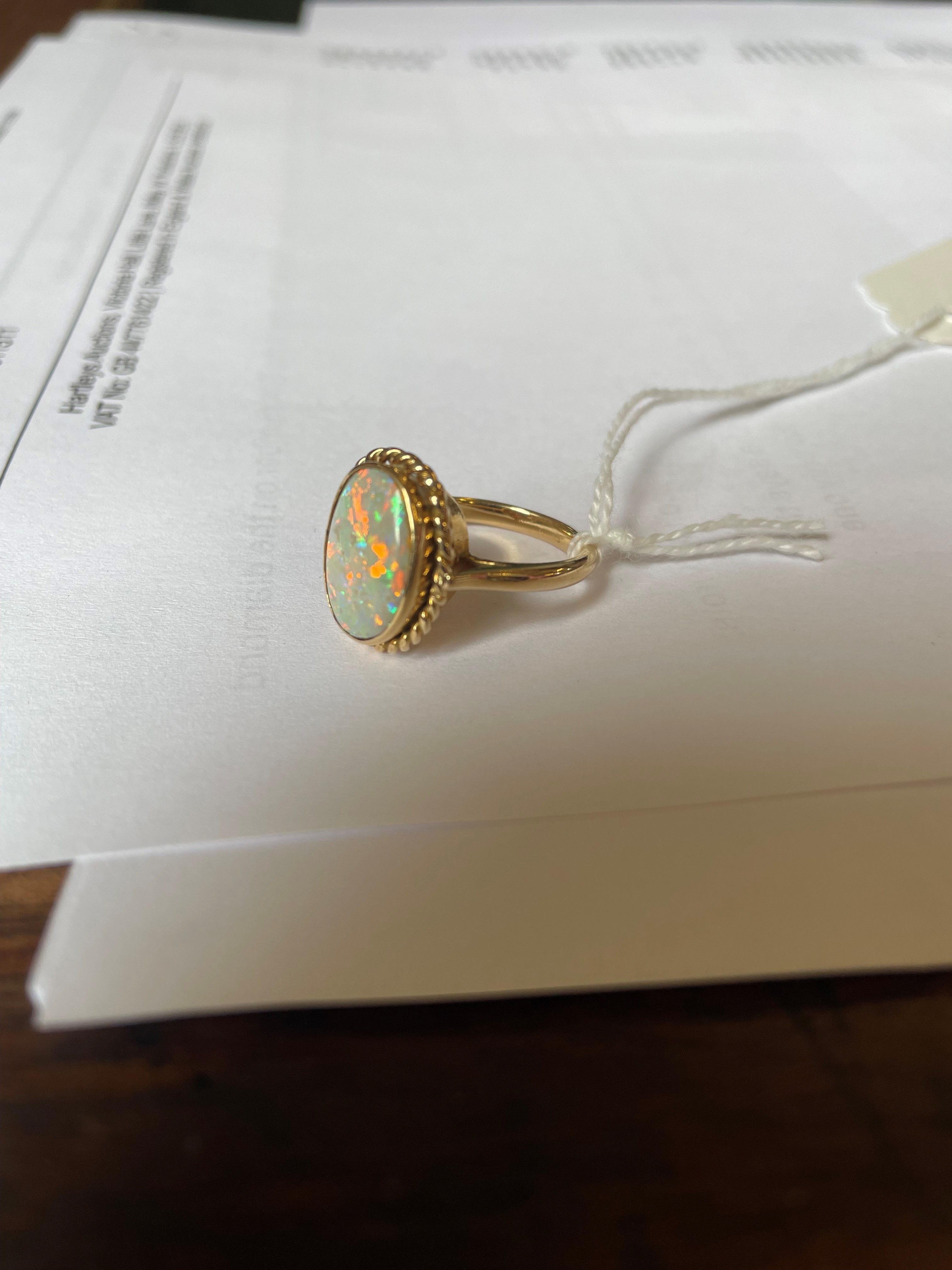 AN OPAL DRESS RING, the oval cabochon polished stone collet set to a rope twist mount and plain Image