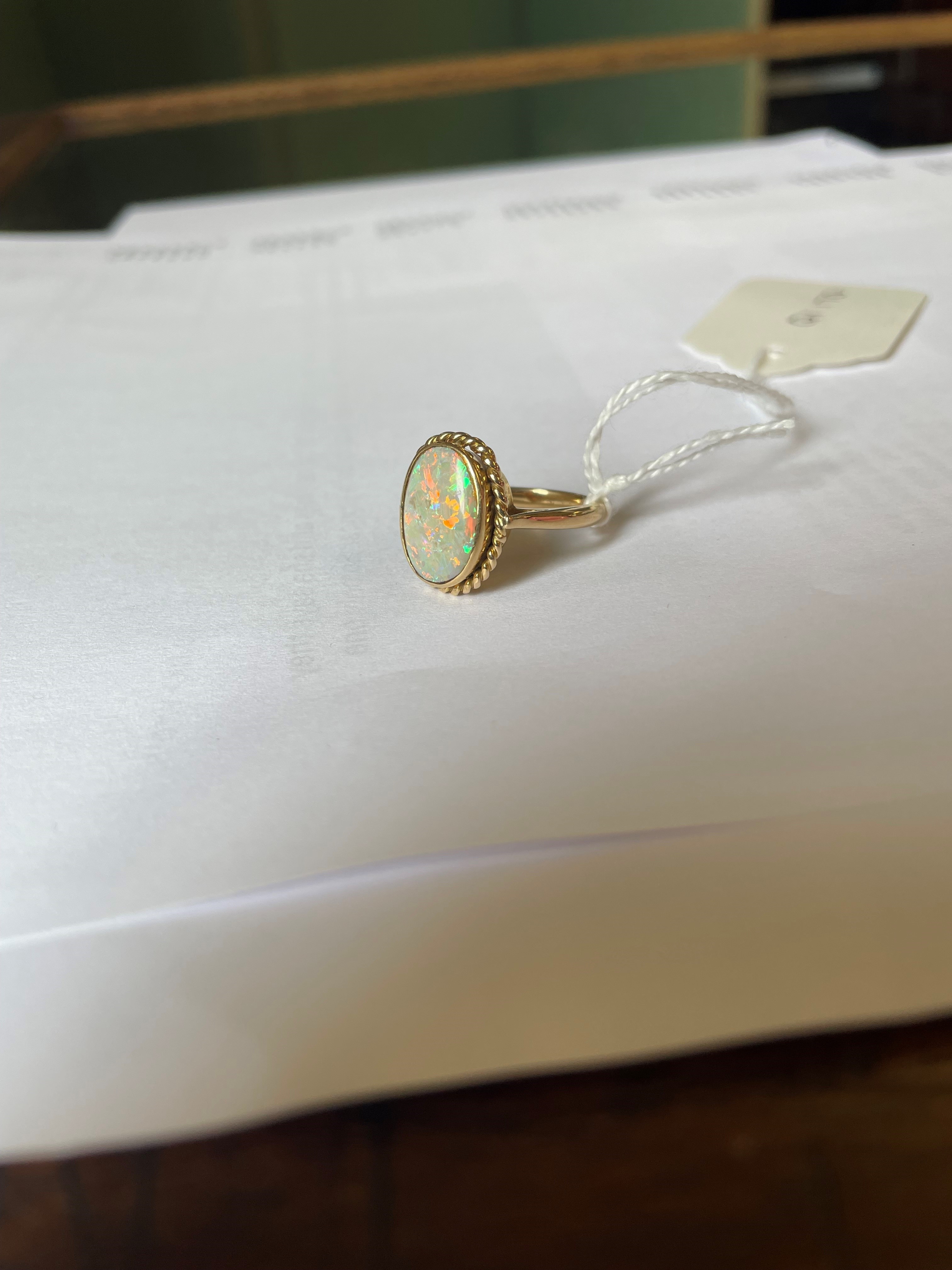 AN OPAL DRESS RING, the oval cabochon polished stone collet set to a rope twist mount and plain Image