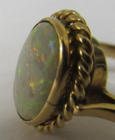 AN OPAL DRESS RING, the oval cabochon polished stone collet set to a rope twist mount and plain Image