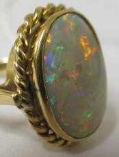 AN OPAL DRESS RING, the oval cabochon polished stone collet set to a rope twist mount and plain Image