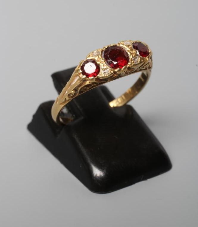 A THREE STONE GARNET RING, the graduated circular stones in carved mount with two pairs of rose cut Image