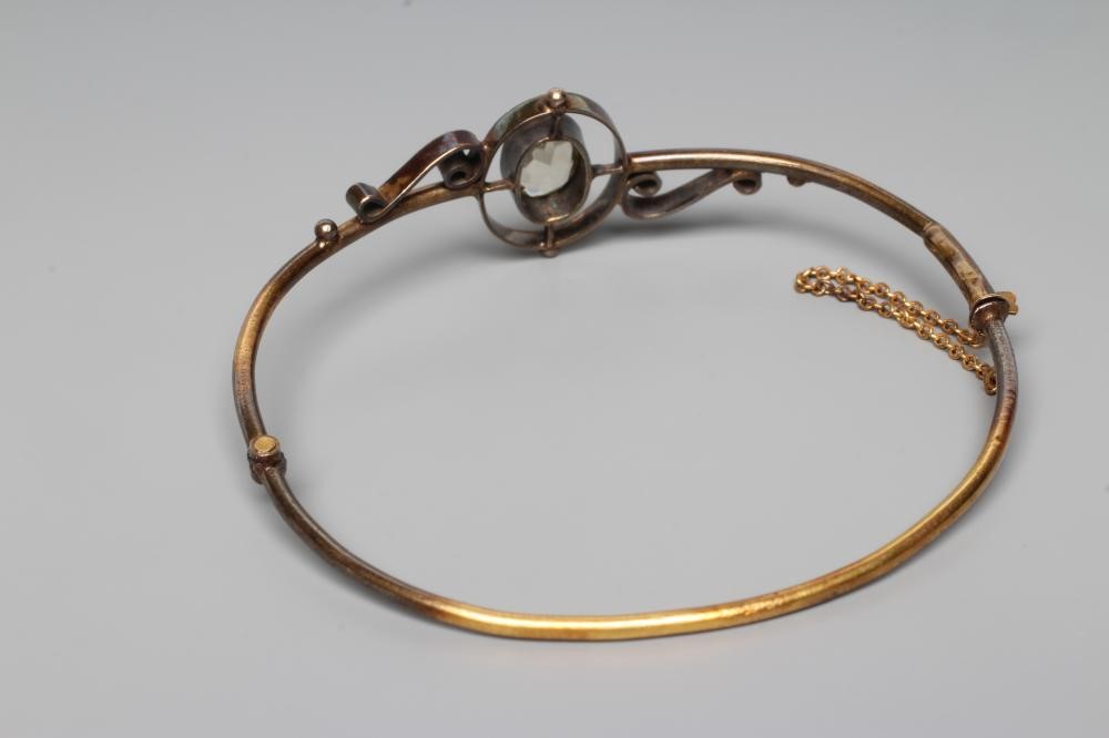 A VICTORIAN STIFF HINGED BANGLE, the upper section centred by an open back collet set oval facet cut Image