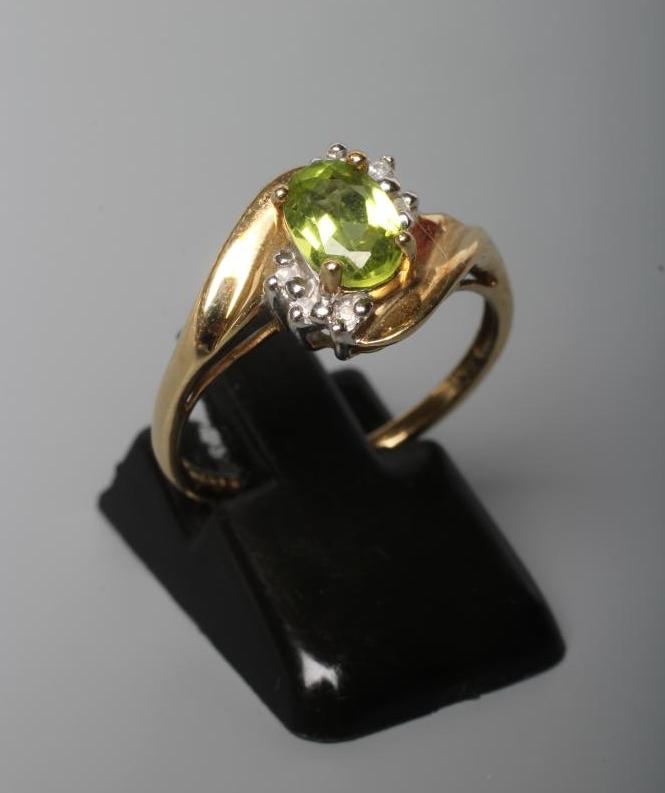 A PERIDOT AND DIAMOND DRESS RING, the oval facet cut peridot claw set within two sets of three point Image