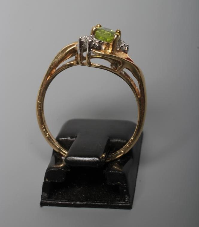 A PERIDOT AND DIAMOND DRESS RING, the oval facet cut peridot claw set within two sets of three point Image