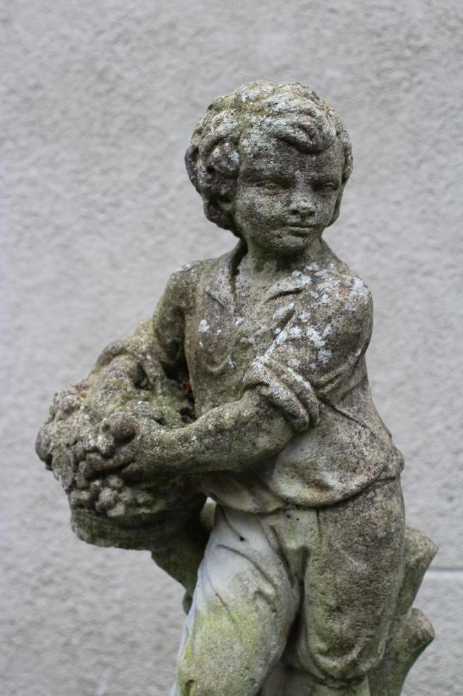 A CAST STONE ALLEGORICAL FIGURE of Autumn, modelled as a youth holding a basket of fruit, raised on Image