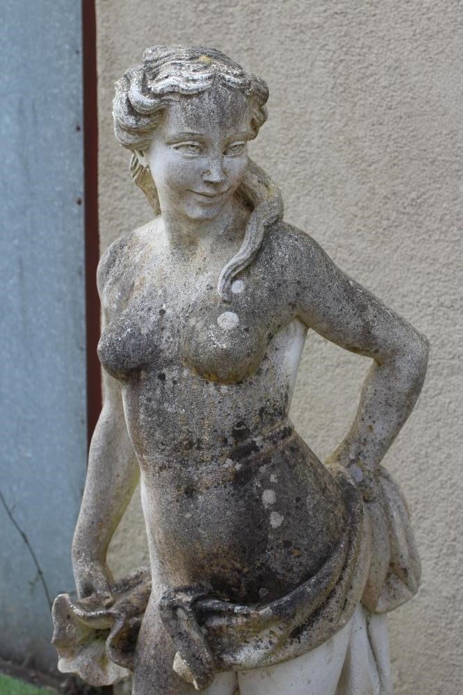 A CAST STONE FIGURE OF A WATER NYMPH, the nude figure standing and holding a shell, another shell at Image