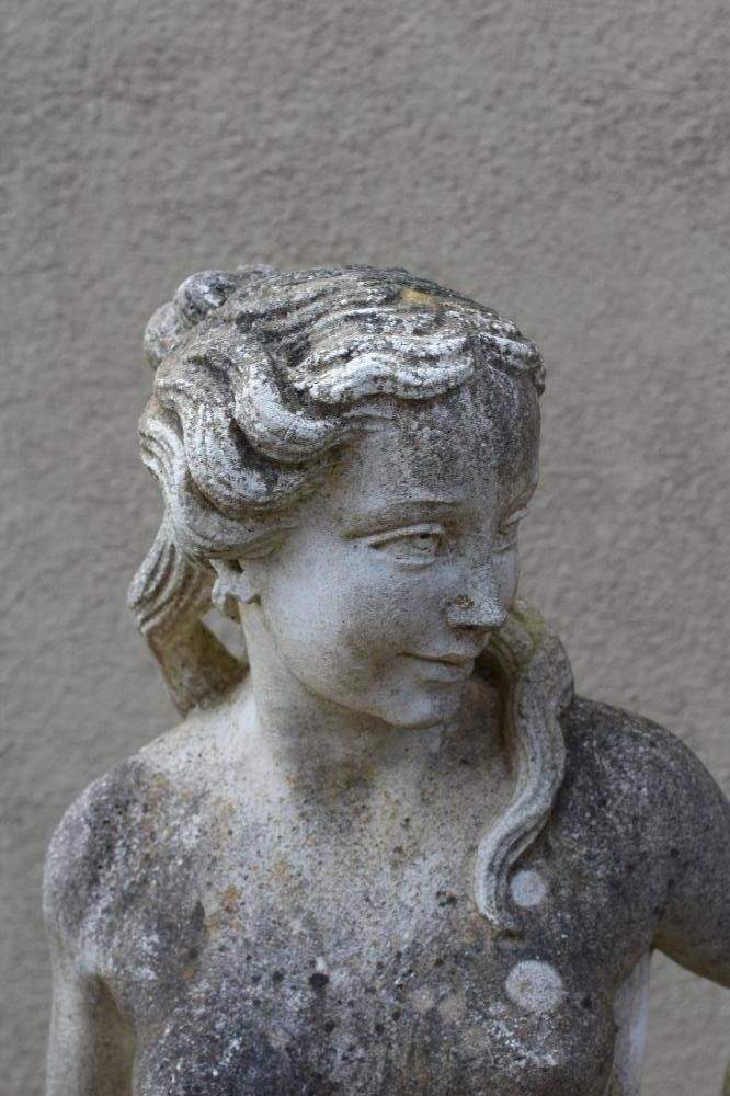 A CAST STONE FIGURE OF A WATER NYMPH, the nude figure standing and holding a shell, another shell at Image