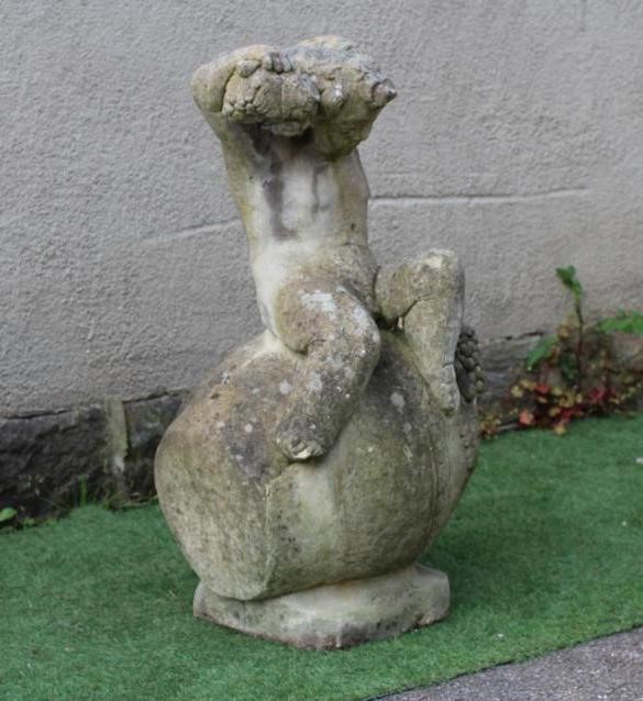 A CAST STONE FIGURE OF A BACCANALIAN PUTTO, modelled seated on an overturned wine jar and holding Image