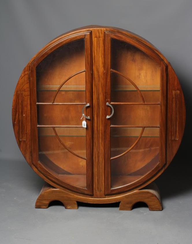AN ART DECO WALNUT DISPLAY CABINET of circular outline with two astragal glazed doors enclosing Image