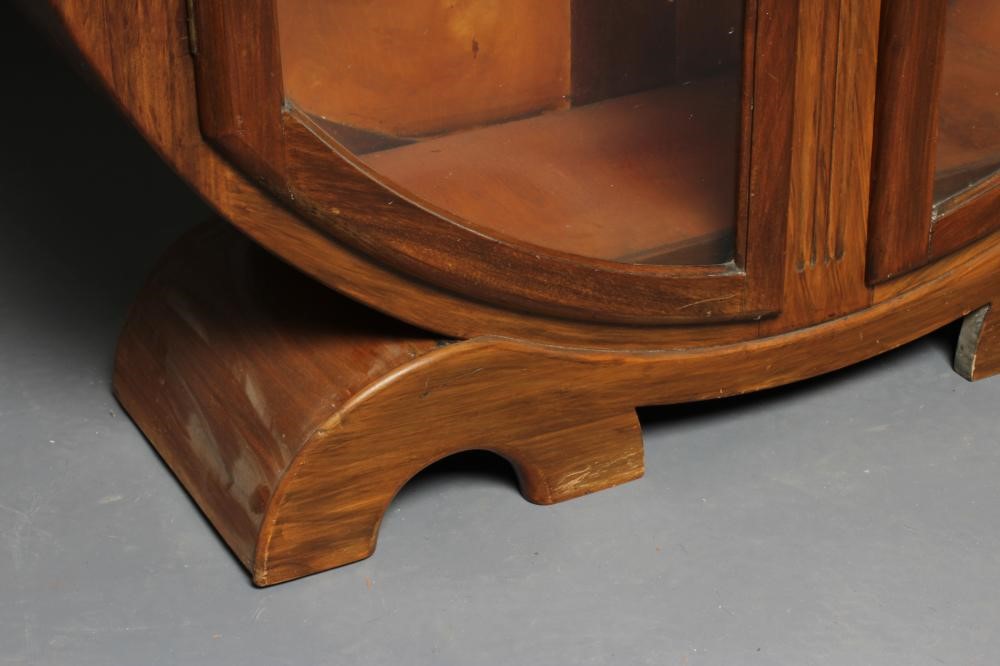 AN ART DECO WALNUT DISPLAY CABINET of circular outline with two astragal glazed doors enclosing Image
