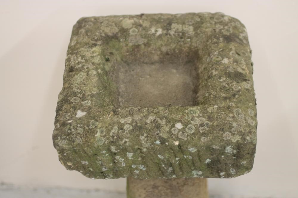 A SANDSTONE BIRD BATH of rough hewn square form with square tapering column and mildly domed base Image