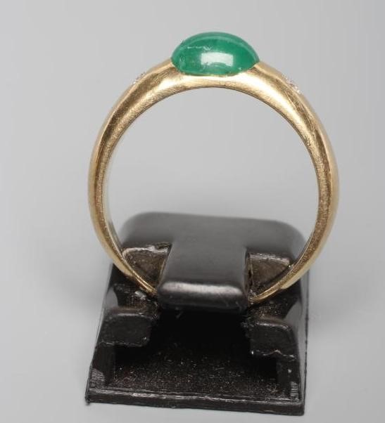 AN EMERALD AND DIAMOND RING, the oval cabochon polished emerald tension set and flanked by two gypsy Image