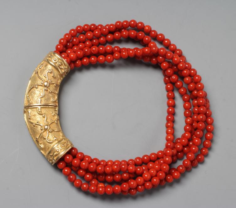 A SIX STRAND CORAL BEAD BRACELET, the strands set into a crescent shaped panel clasp chased with Image