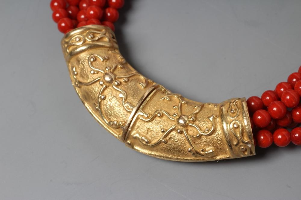 A SIX STRAND CORAL BEAD BRACELET, the strands set into a crescent shaped panel clasp chased with Image