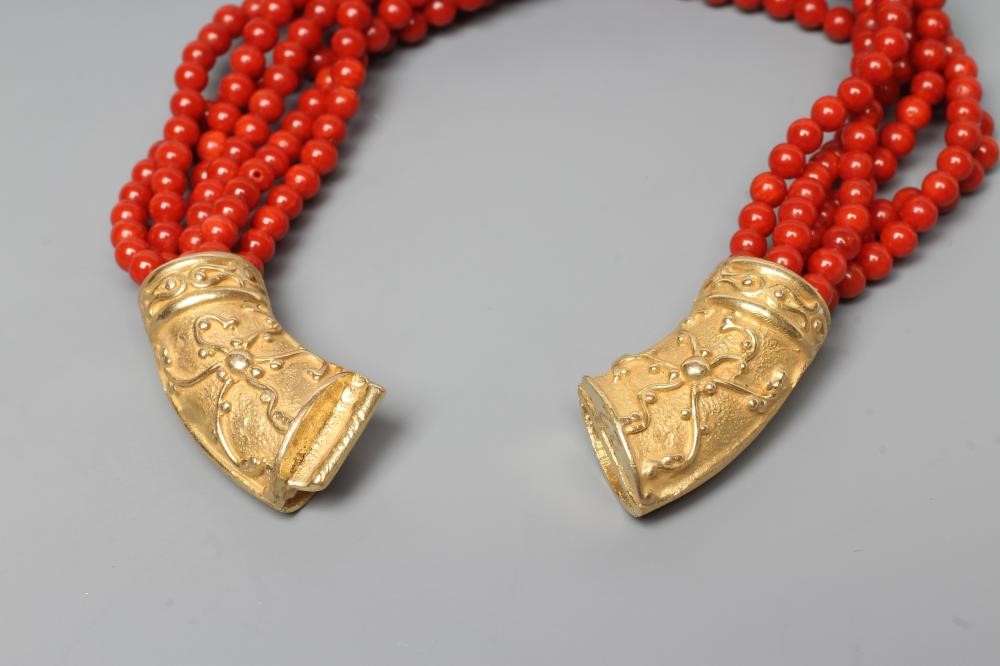A SIX STRAND CORAL BEAD BRACELET, the strands set into a crescent shaped panel clasp chased with Image