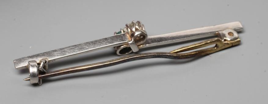 AN EMERALD AND DIAMOND BAR BROOCH, the circular facet cut stones claw set to an asymetrical knife Image