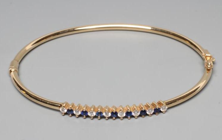 A STIFF HINGED BANGLE, the upper section claw set with seven small sapphires and eight diamonds, to Image