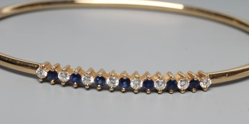 A STIFF HINGED BANGLE, the upper section claw set with seven small sapphires and eight diamonds, to Image