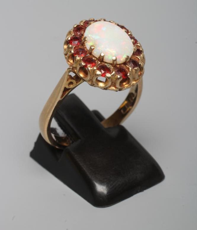 AN OPAL AND GARNET CLUSTER RING, the oval cabochon polished opal claw set to a border of small facet Image