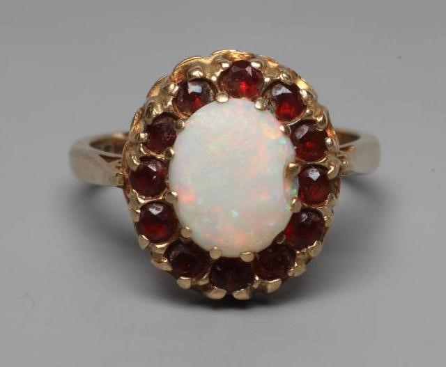 AN OPAL AND GARNET CLUSTER RING, the oval cabochon polished opal claw set to a border of small facet Image