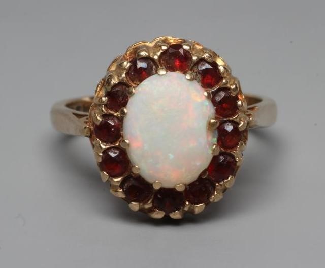 AN OPAL AND GARNET CLUSTER RING, the oval cabochon polished opal claw set to a border of small facet Image