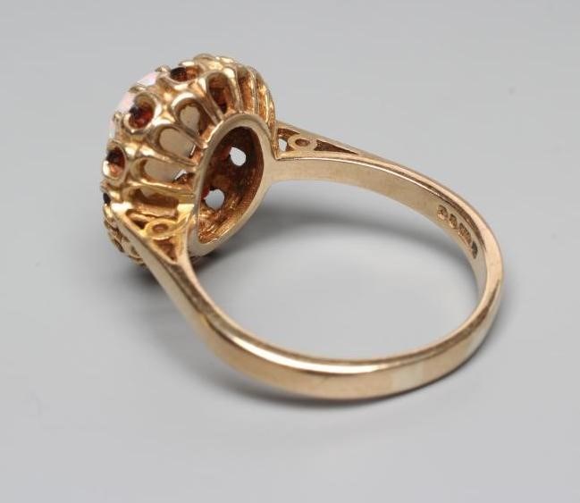 AN OPAL AND GARNET CLUSTER RING, the oval cabochon polished opal claw set to a border of small facet Image
