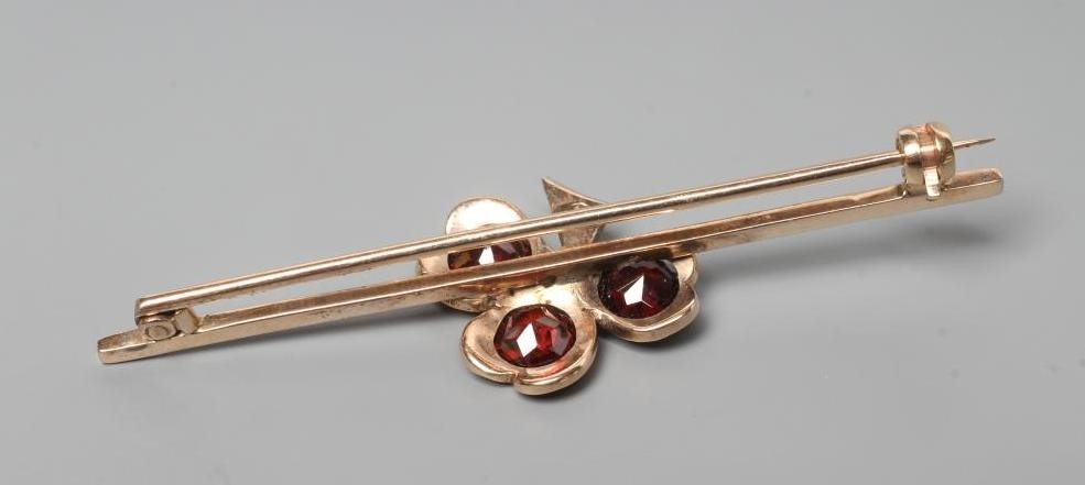 A SHAMROCK BAR BROOCH set with three facet cut circular garnets with small diamond centre and stem, Image