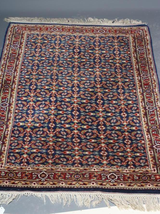 A PERSIAN RUG, the navy blue field with repeating pattern of foliate scrolls and flower heads, the Image