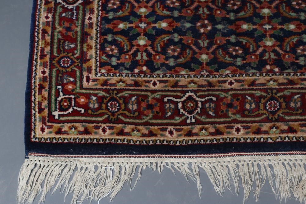 A PERSIAN RUG, the navy blue field with repeating pattern of foliate scrolls and flower heads, the Image