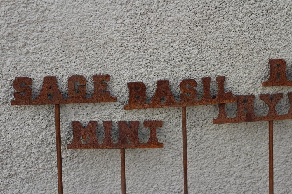 A SET OF TEN RECLAIMED METAL HERB LABELS, each on a turned post with rust patination, 6" - 13" x 37 Image