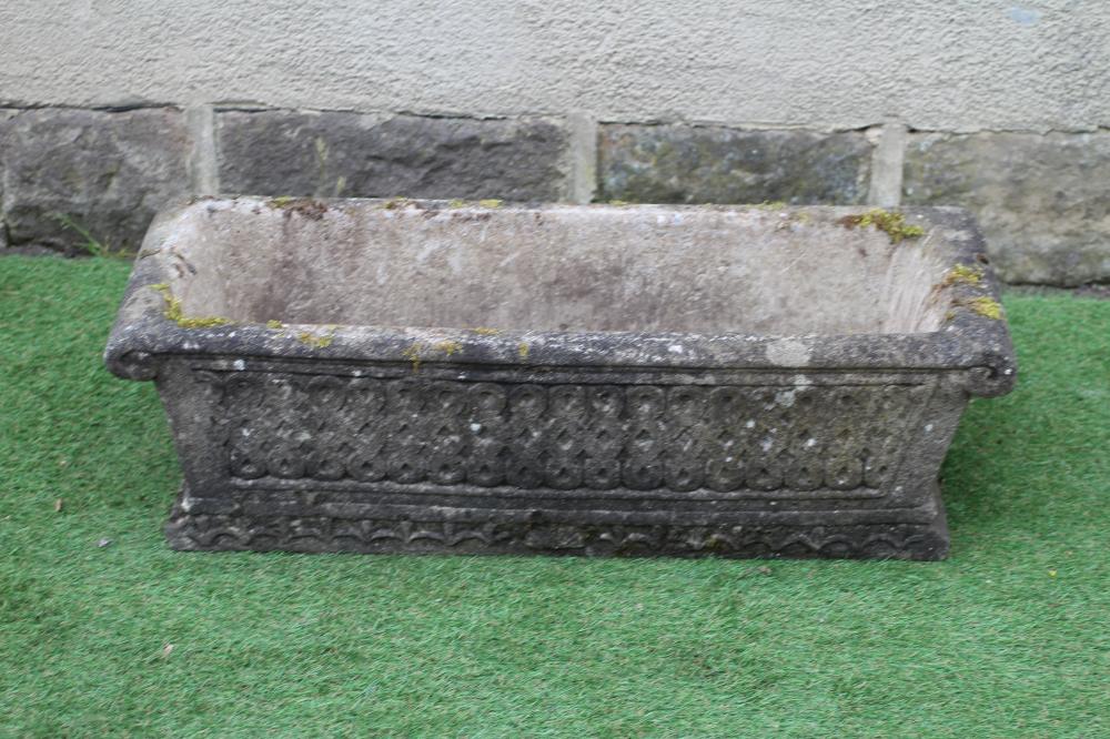 A CAST STONE JARDINIERE of oblong tapering form with scrolled rim and flared base, the sides moulded Image