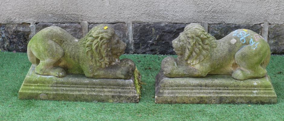 A PAIR OF CAST STONE RECUMBENT LIONS each holding a ball in its front paws, on moulded oblong base, Image