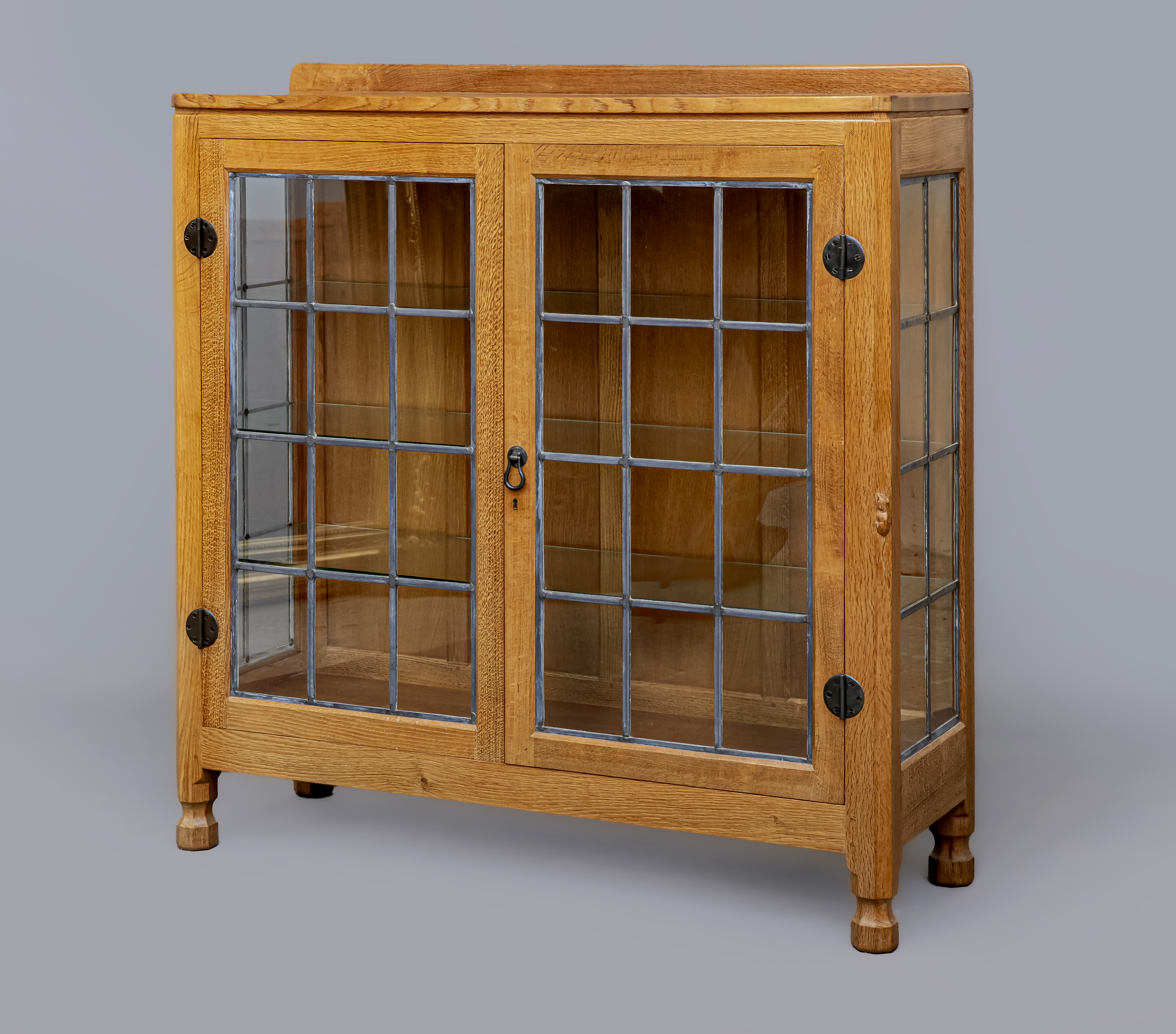 A ROBERT THOMPSON ADZED OAK DISPLAY CABINET of canted oblong form with leaded glazed doors and sides Image