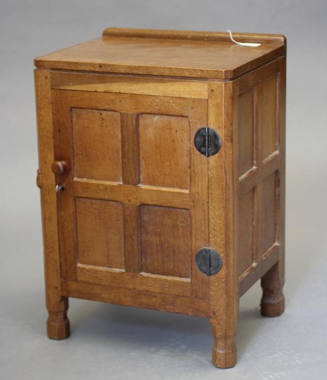 A ROBERT THOMPSON ADZED OAK BEDSIDE CABINET of canted multi-panelled oblong form Image