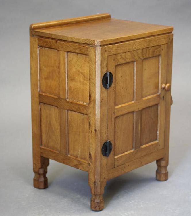 A ROBERT THOMPSON ADZED OAK BEDSIDE CABINET of canted multi-panelled oblong form Image
