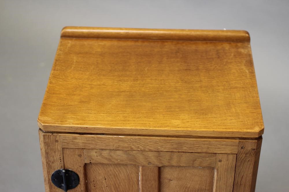 A ROBERT THOMPSON ADZED OAK BEDSIDE CABINET of canted multi-panelled oblong form Image