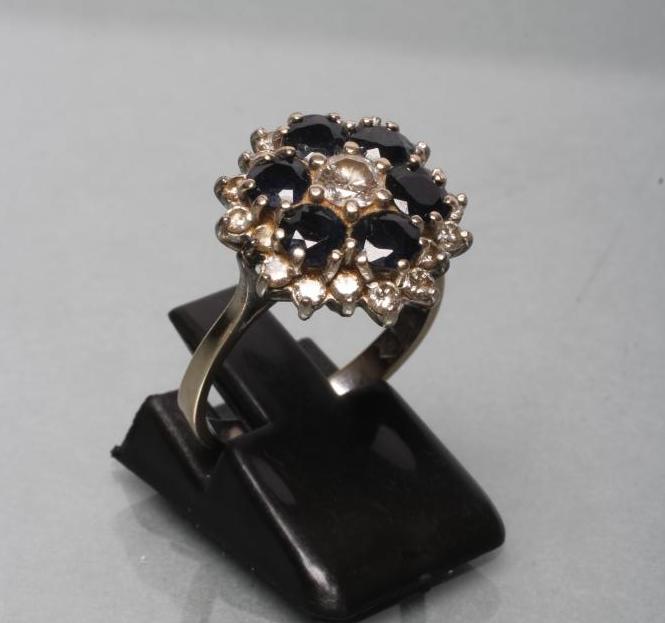 A SAPPHIRE AND DIAMOND CLUSTER RING claw set with six round facet cut claw set sapphires within a Image