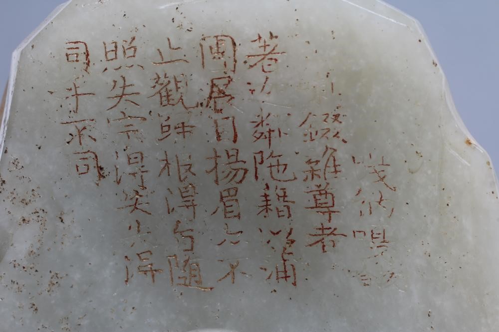 A CHINESE JADE DEITY seated before rockwork with engraved and stained red and gilt script Image