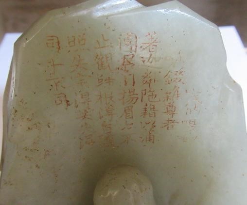 A CHINESE JADE DEITY seated before rockwork with engraved and stained red and gilt script Image