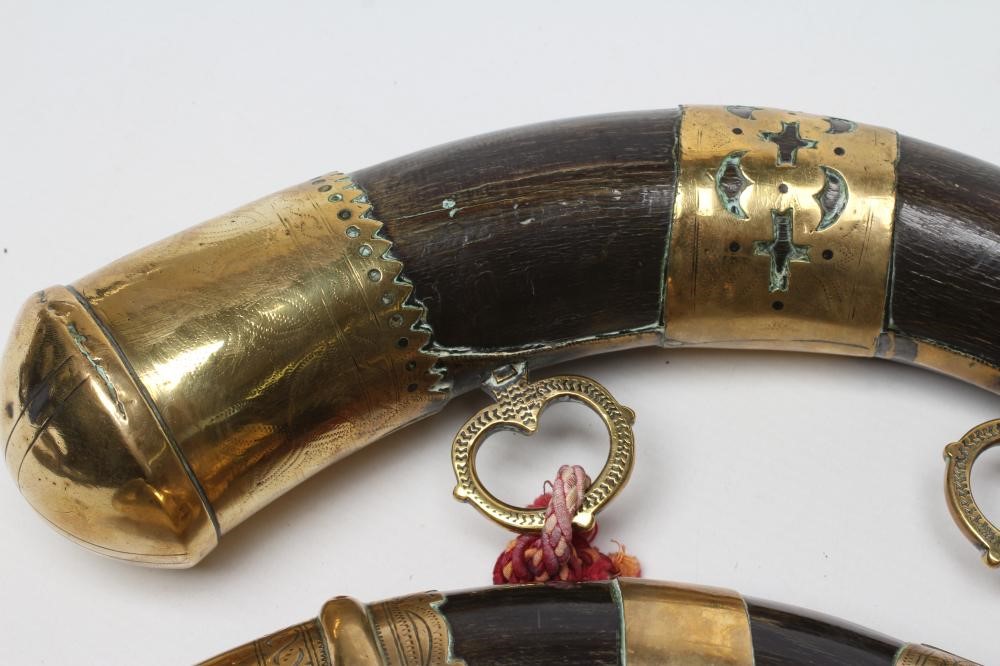 A MATCHED PAIR OF BRASS MOUNTED HORN POWDER FLASKS both with highly decorated metal work and twin Image