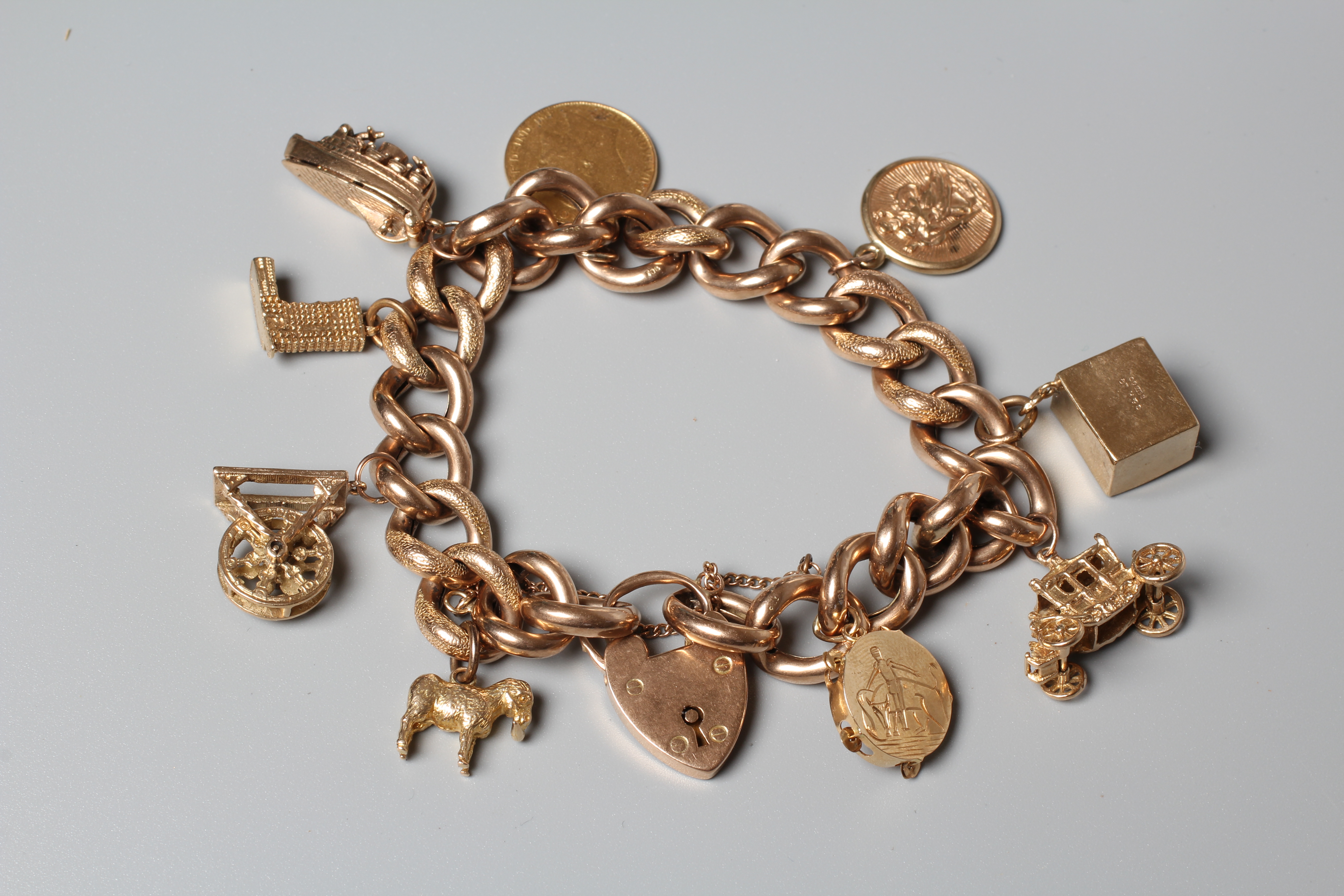 A CURB LINK BRACELET, the foliate engrved links hung with nine charms including a hard mounted 1910 Image