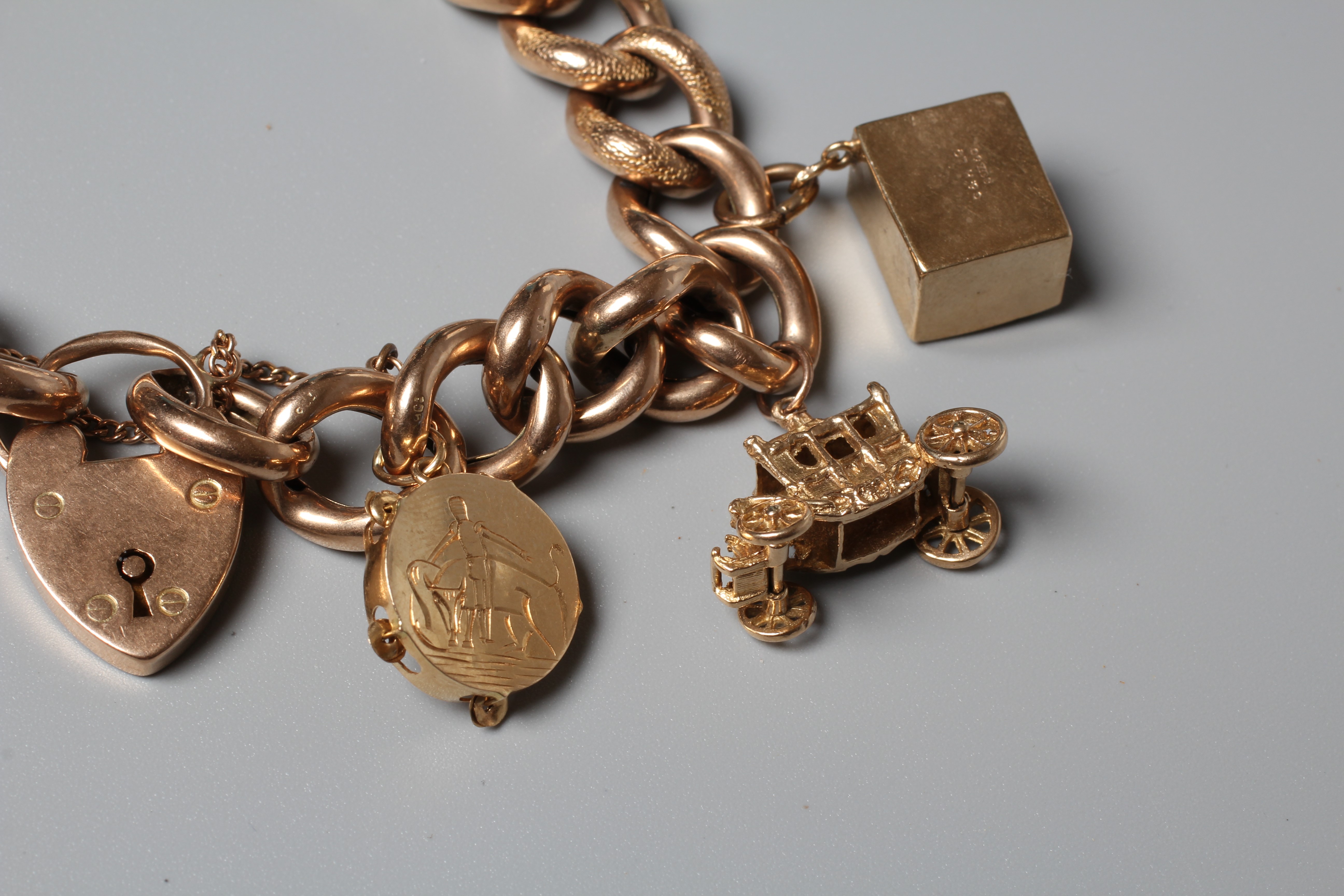 A CURB LINK BRACELET, the foliate engrved links hung with nine charms including a hard mounted 1910 Image