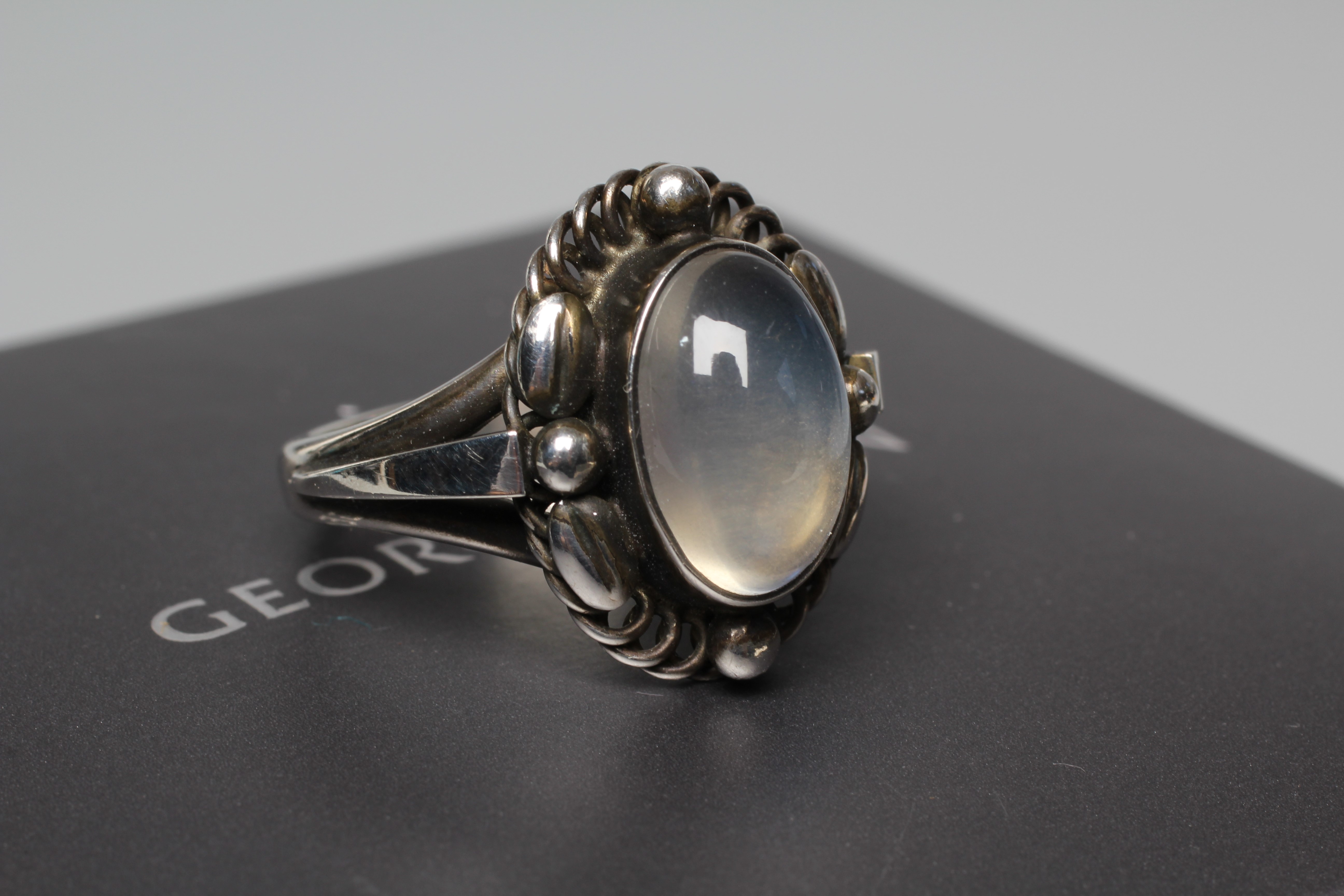 A GEORG JENSEN SILVER SEED AND POD RING collet set with an oval polished moonstone cabochon, stamped Image