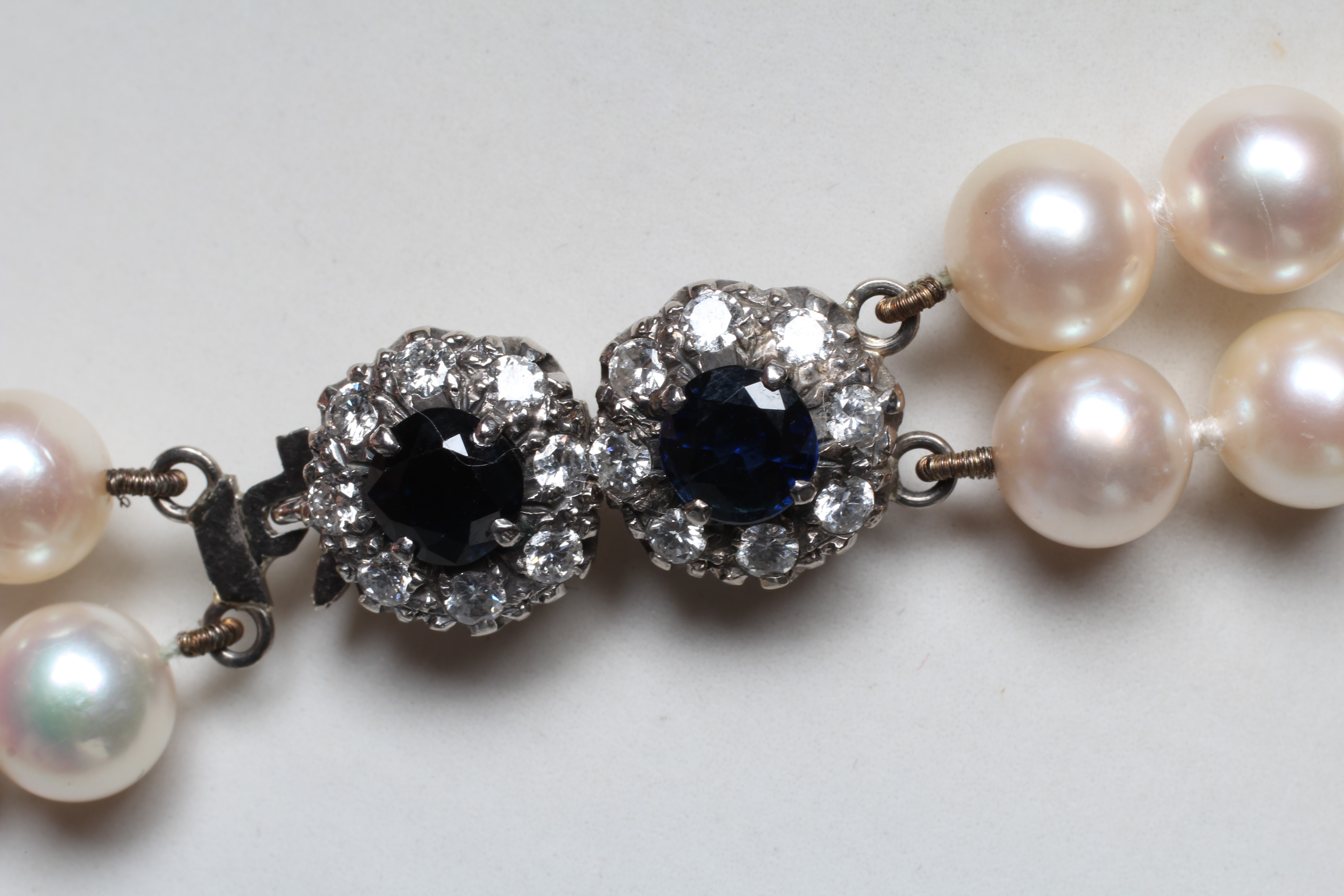 A DOUBLE STRAND CULTURED PEARL CHOKER, set to an unmarked white metal clasp with two sapphire and Image
