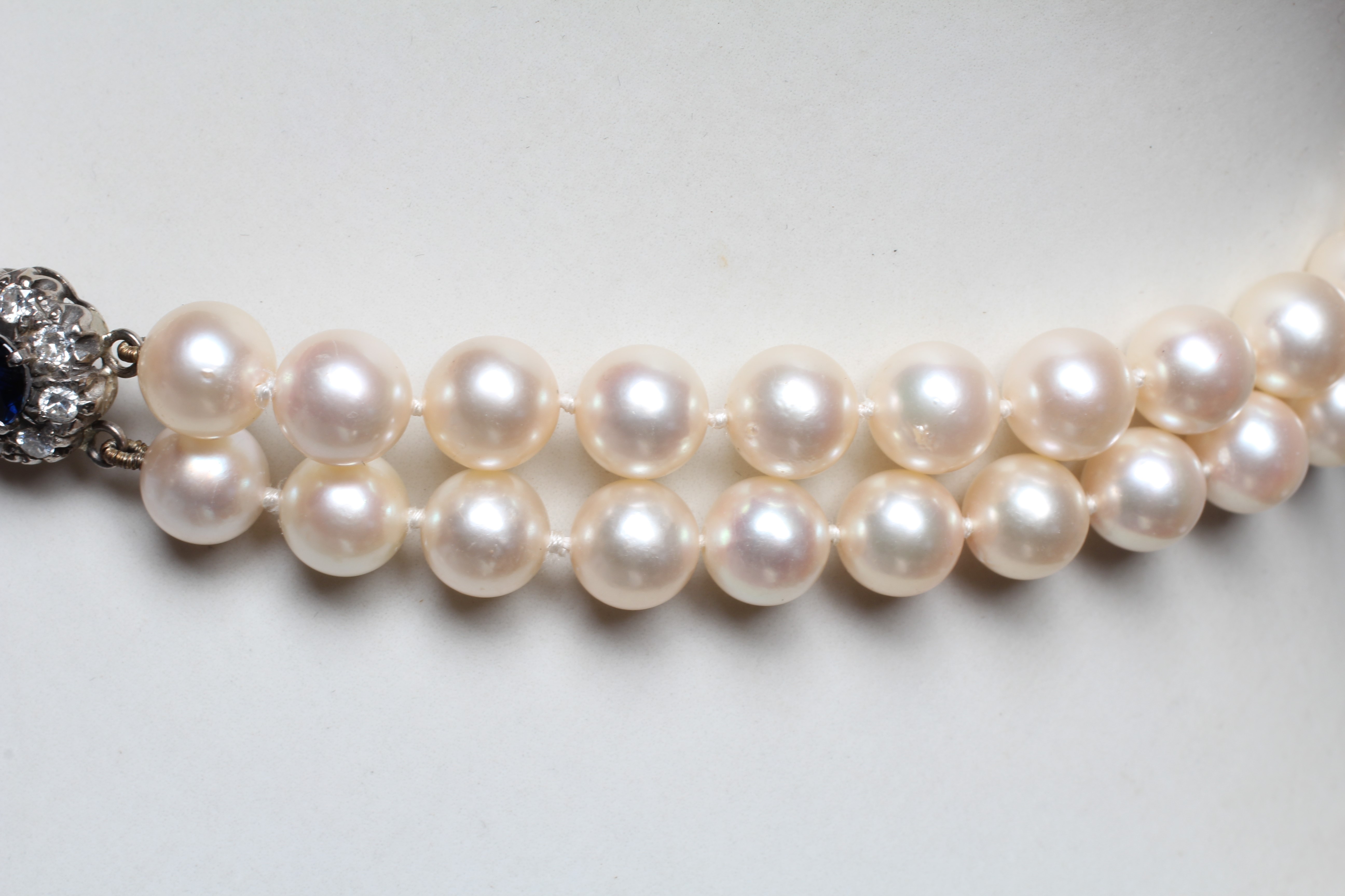 A DOUBLE STRAND CULTURED PEARL CHOKER, set to an unmarked white metal clasp with two sapphire and Image