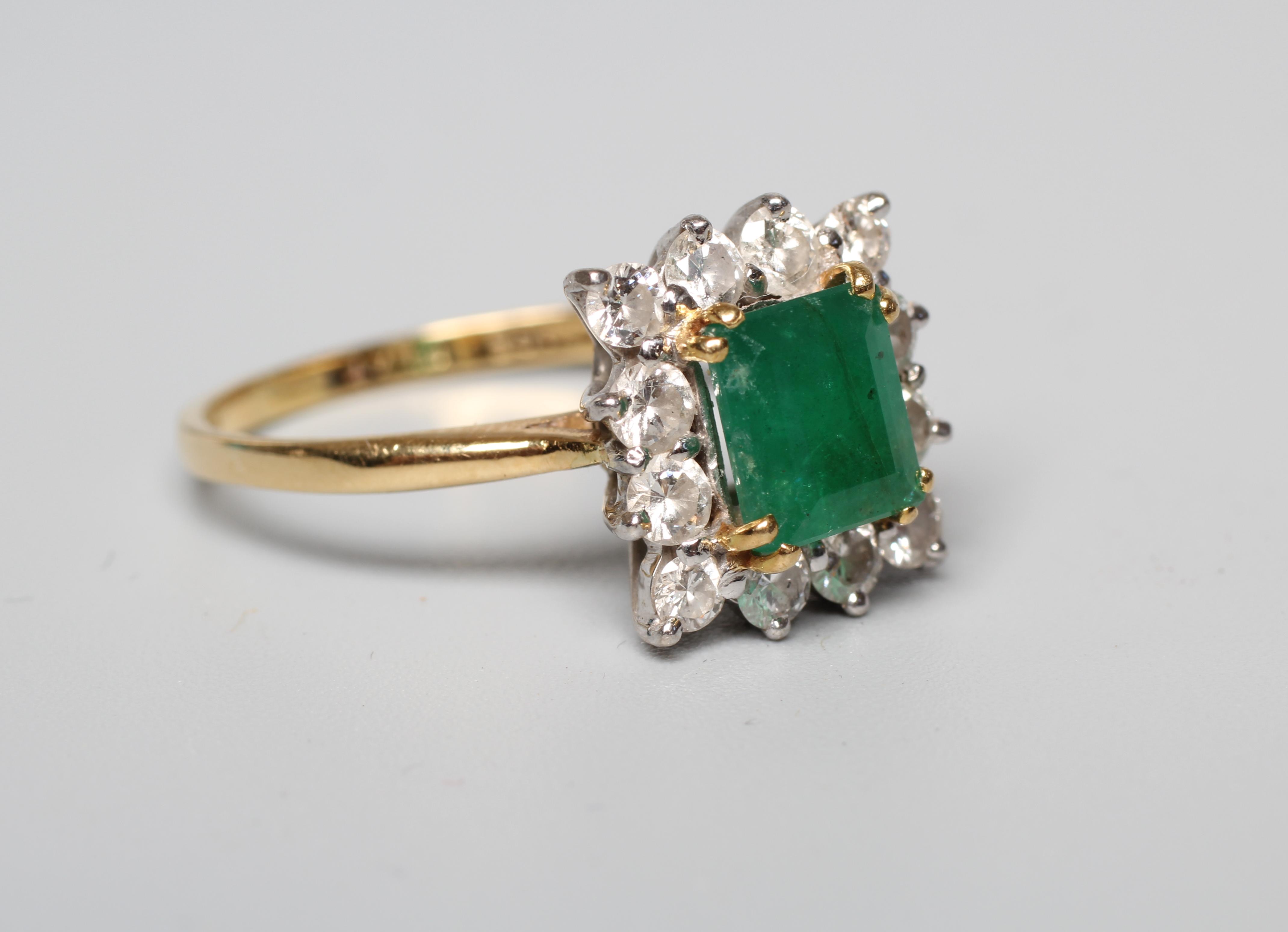AN EMERALD AND DIAMOND CLUSTER RING, the step cut emerald claw set to a border of twelve round Image