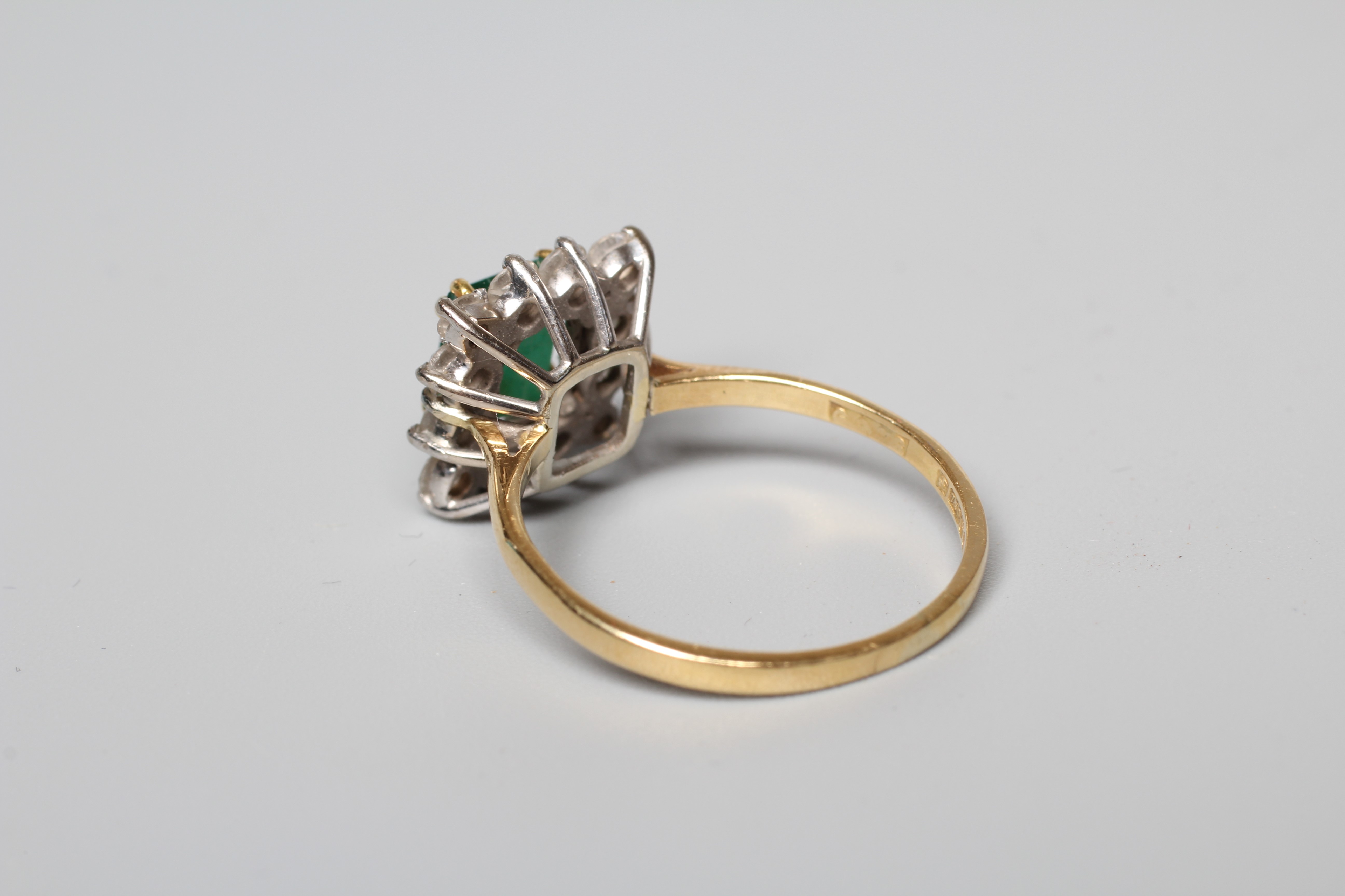 AN EMERALD AND DIAMOND CLUSTER RING, the step cut emerald claw set to a border of twelve round Image