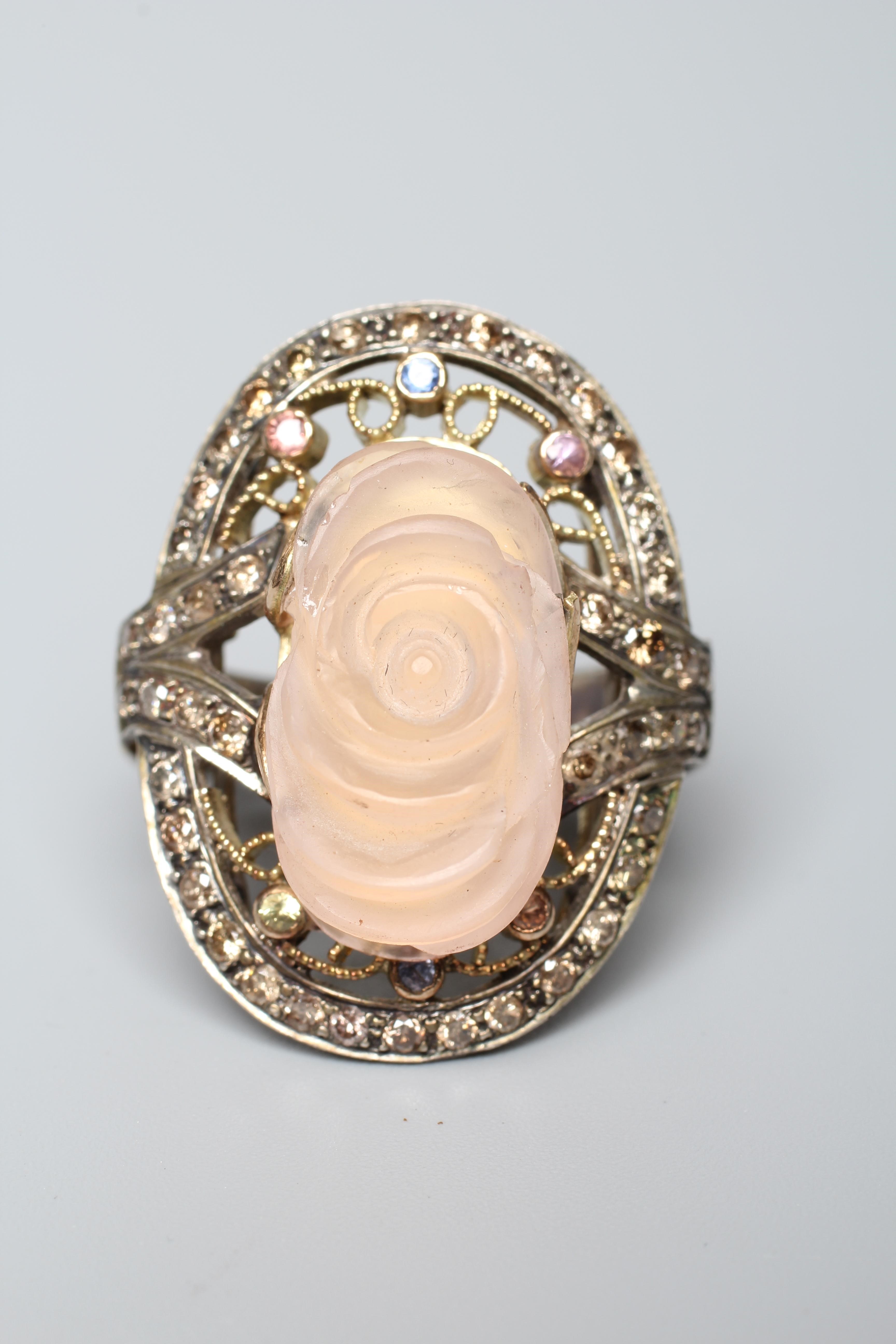 A ROSE QUARTZ COCKTAIL RING, the oval rose head cut stone claw set to an open surround with white Image