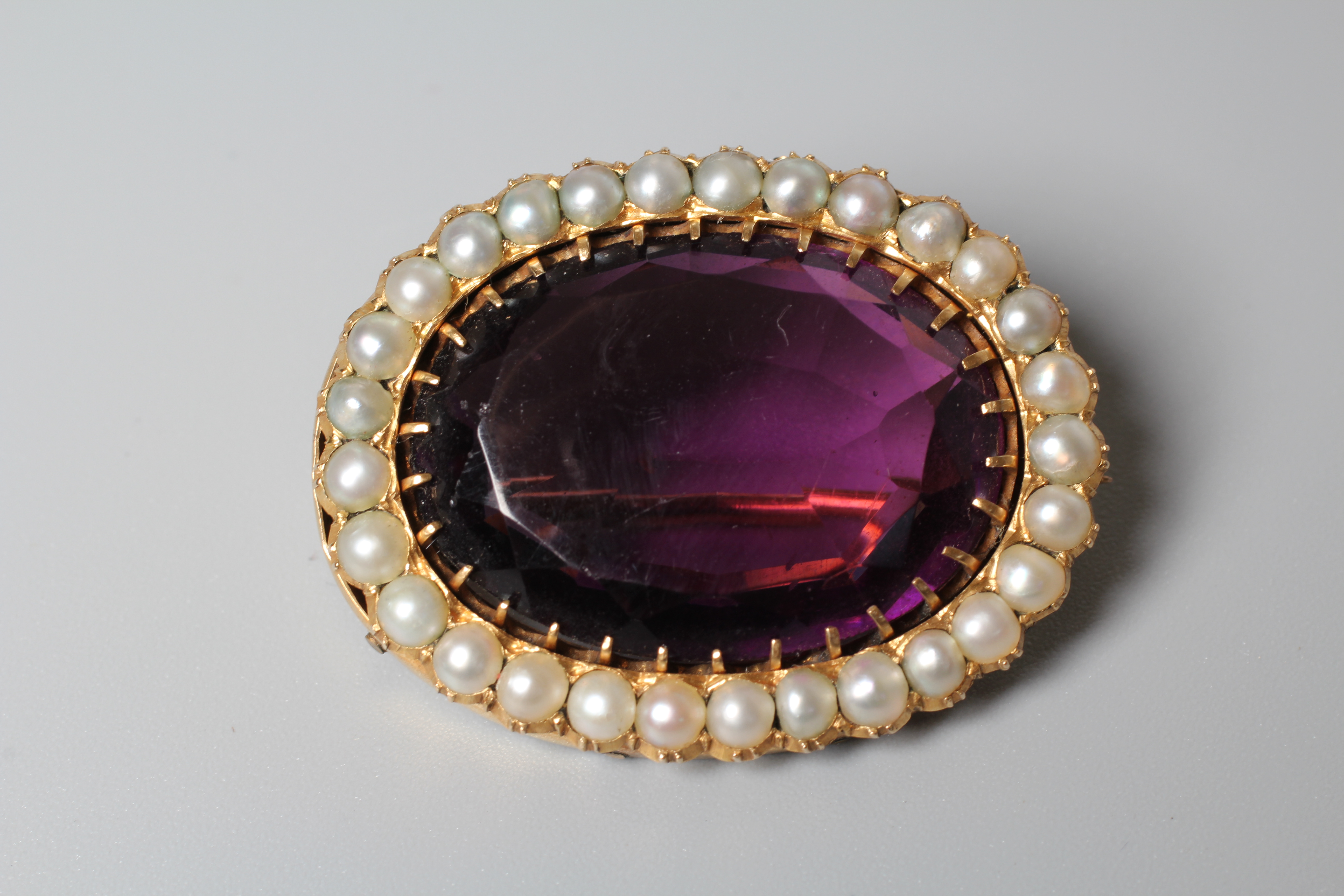A VICTORIAN AMETHYST BROOCH, the oval facet cut stone claw set to a border of small pearls to an Image