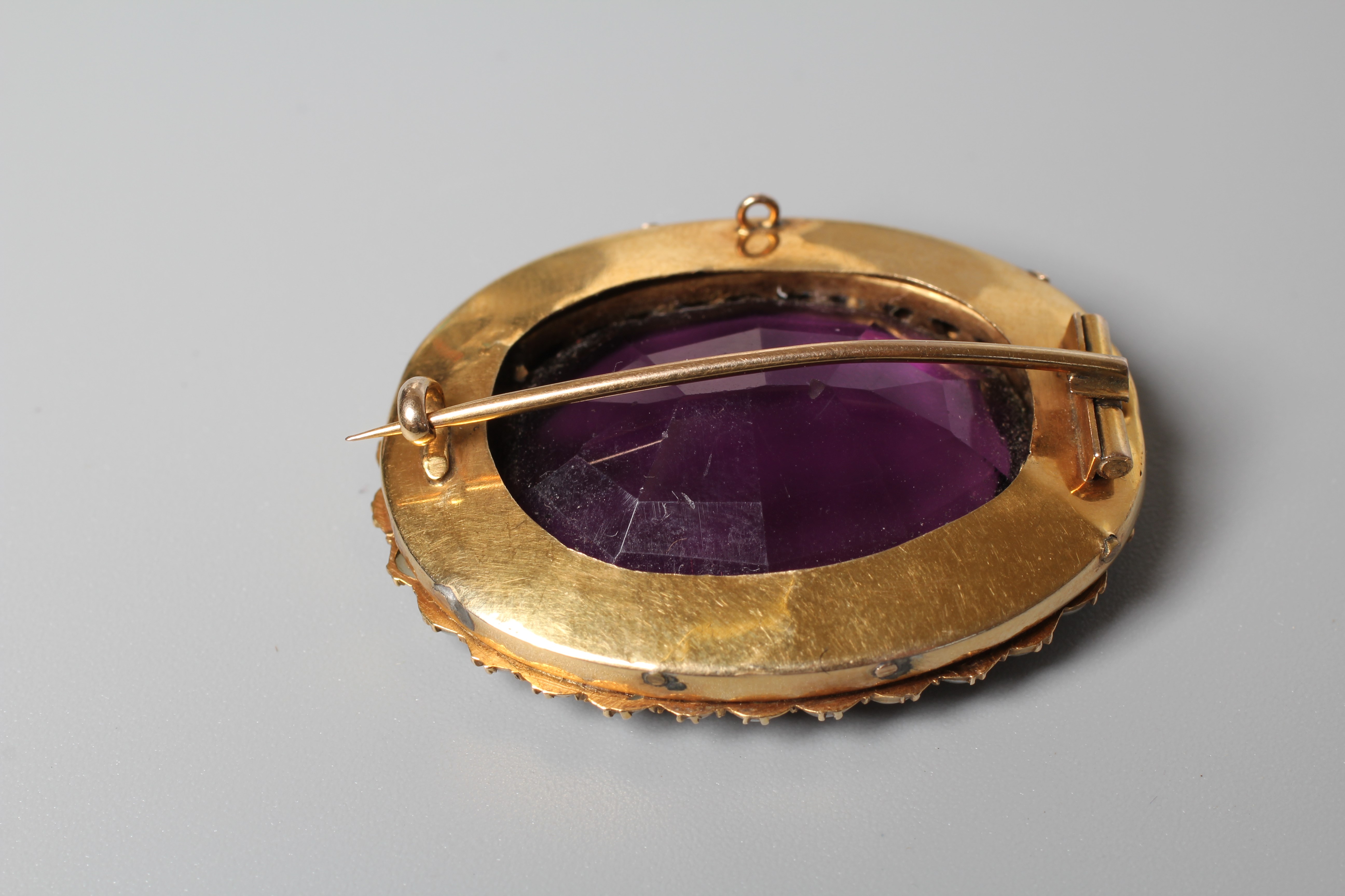 A VICTORIAN AMETHYST BROOCH, the oval facet cut stone claw set to a border of small pearls to an Image